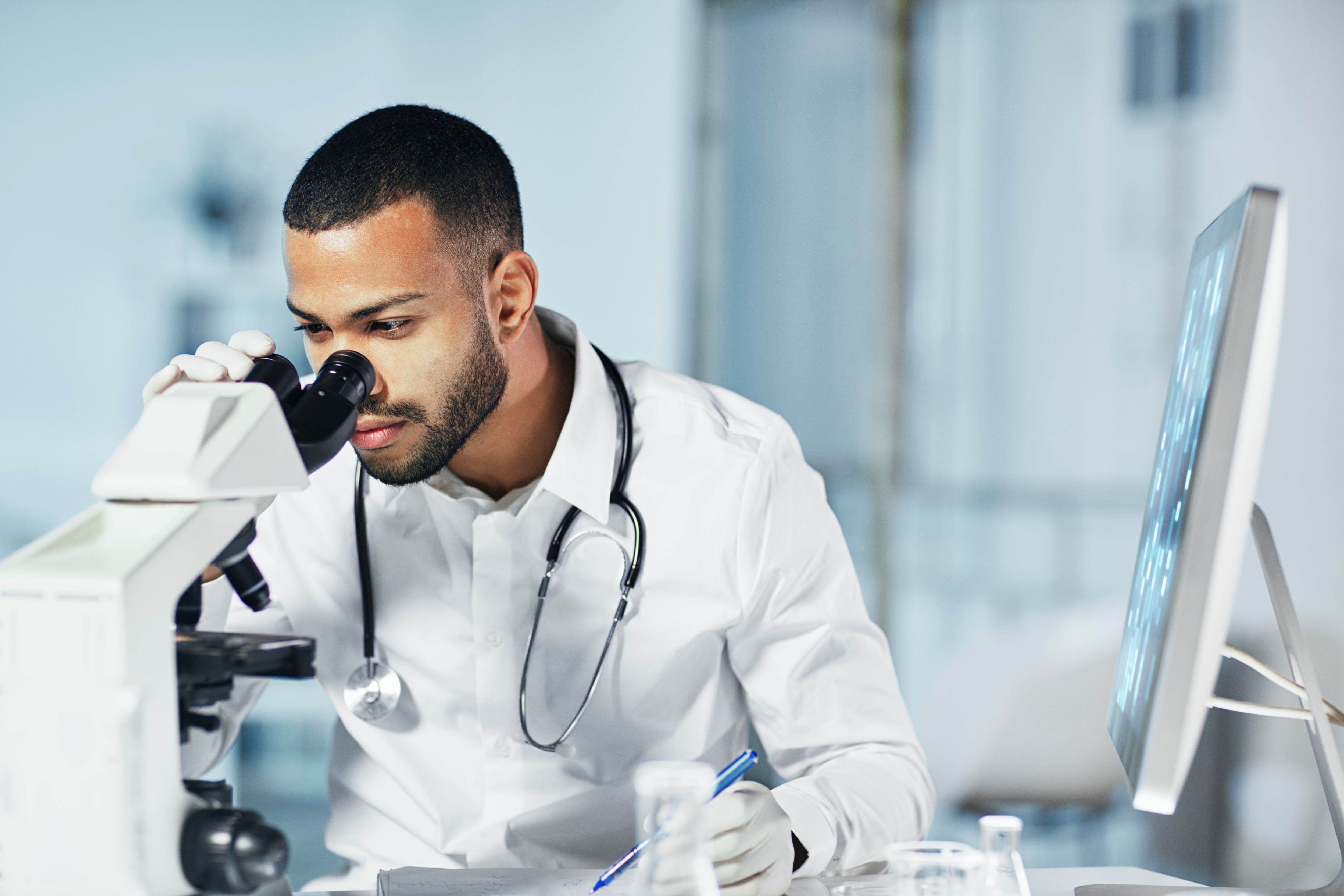 Young scientist wearing a stethoscope around his neck looking through a microscope in the lab.